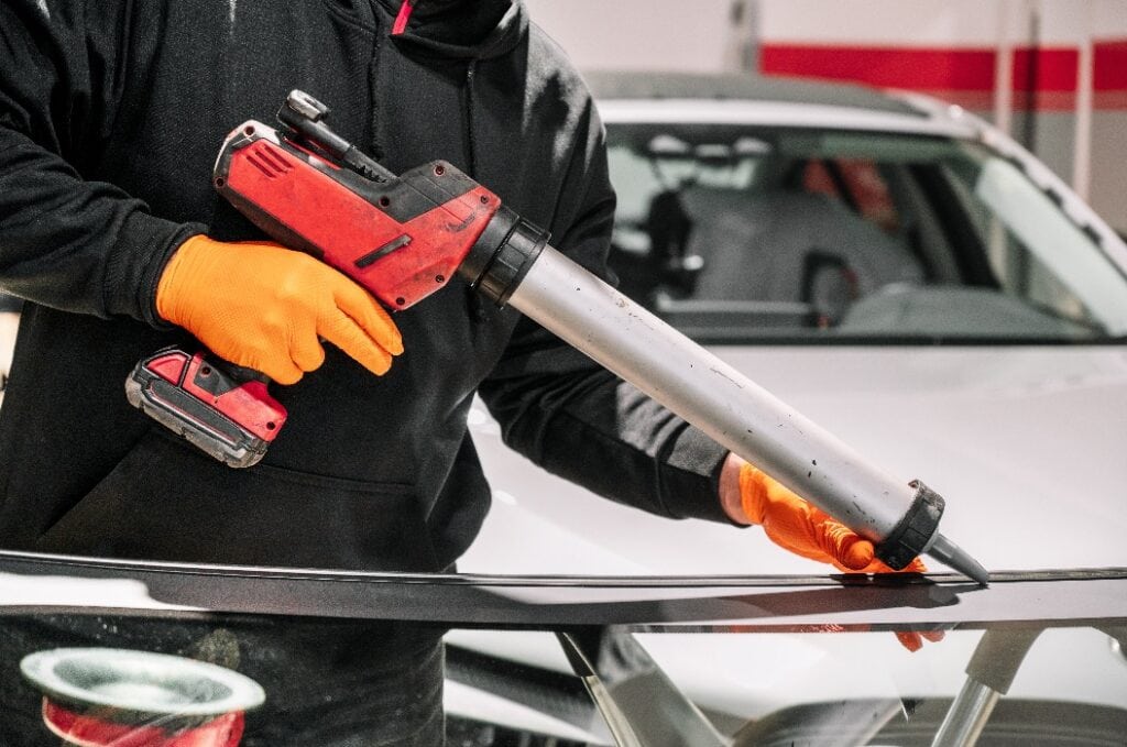 Glazier applying rubber sealing to windshield in garage, close up. High quality photo