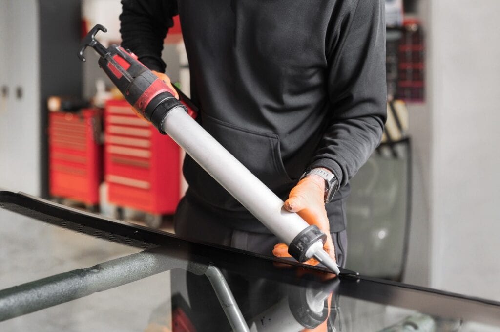 Glazier applying rubber sealing to windshield in garage, close up. High quality photo