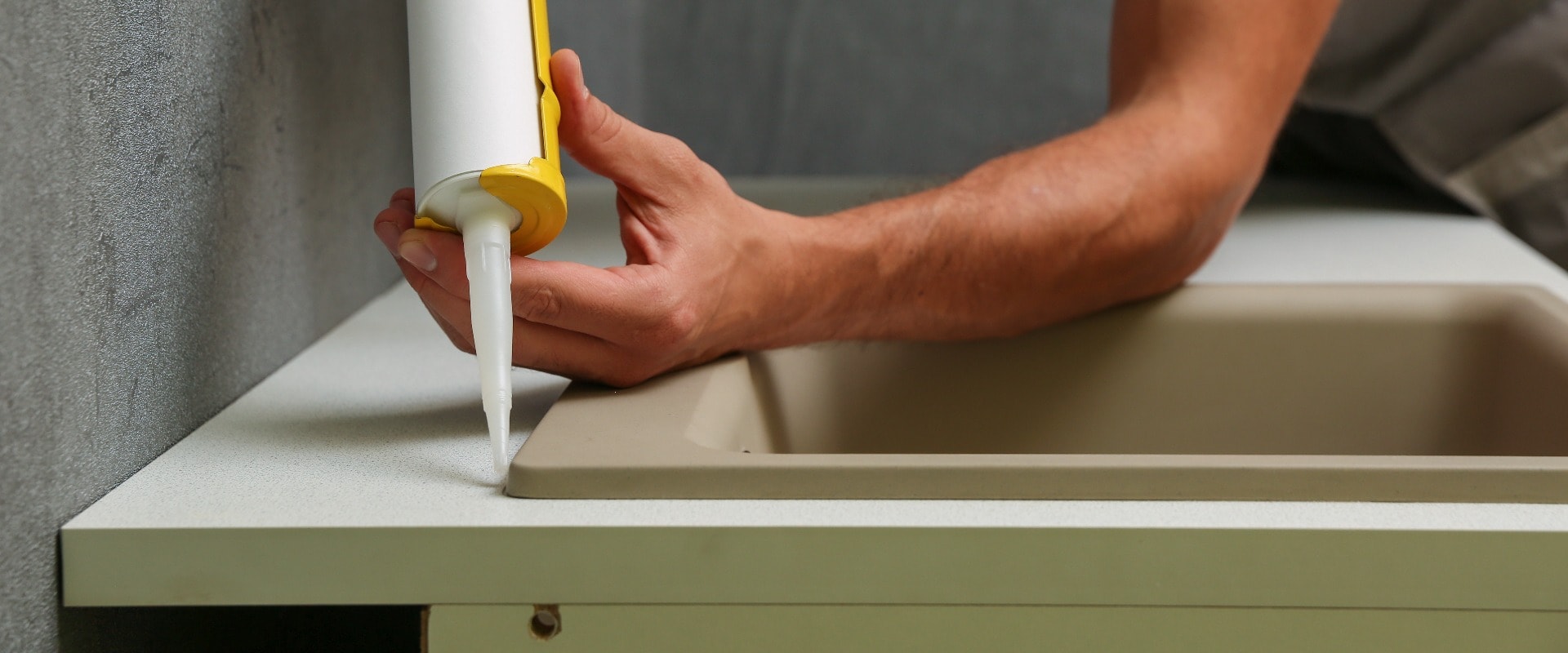 worker seals kitchen sink with sealant. hands of worker works with construction sealant gun in the kitchen.