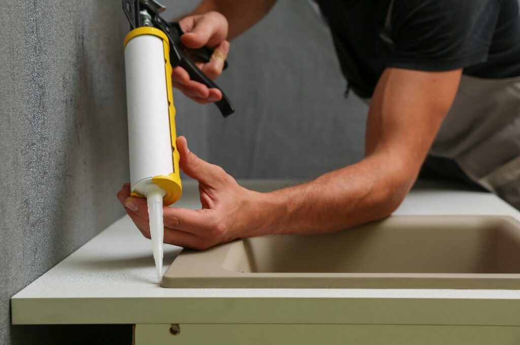 worker seals kitchen sink with sealant. hands of worker works with construction sealant gun in the kitchen.